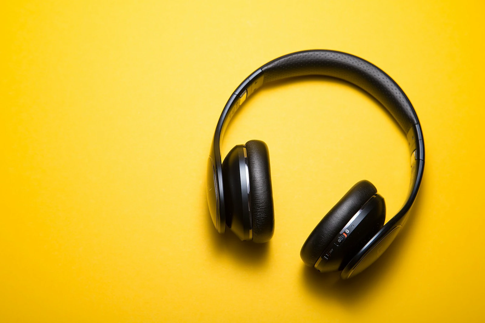 Headphone nirkabel hitam di depan latar kuning cerah