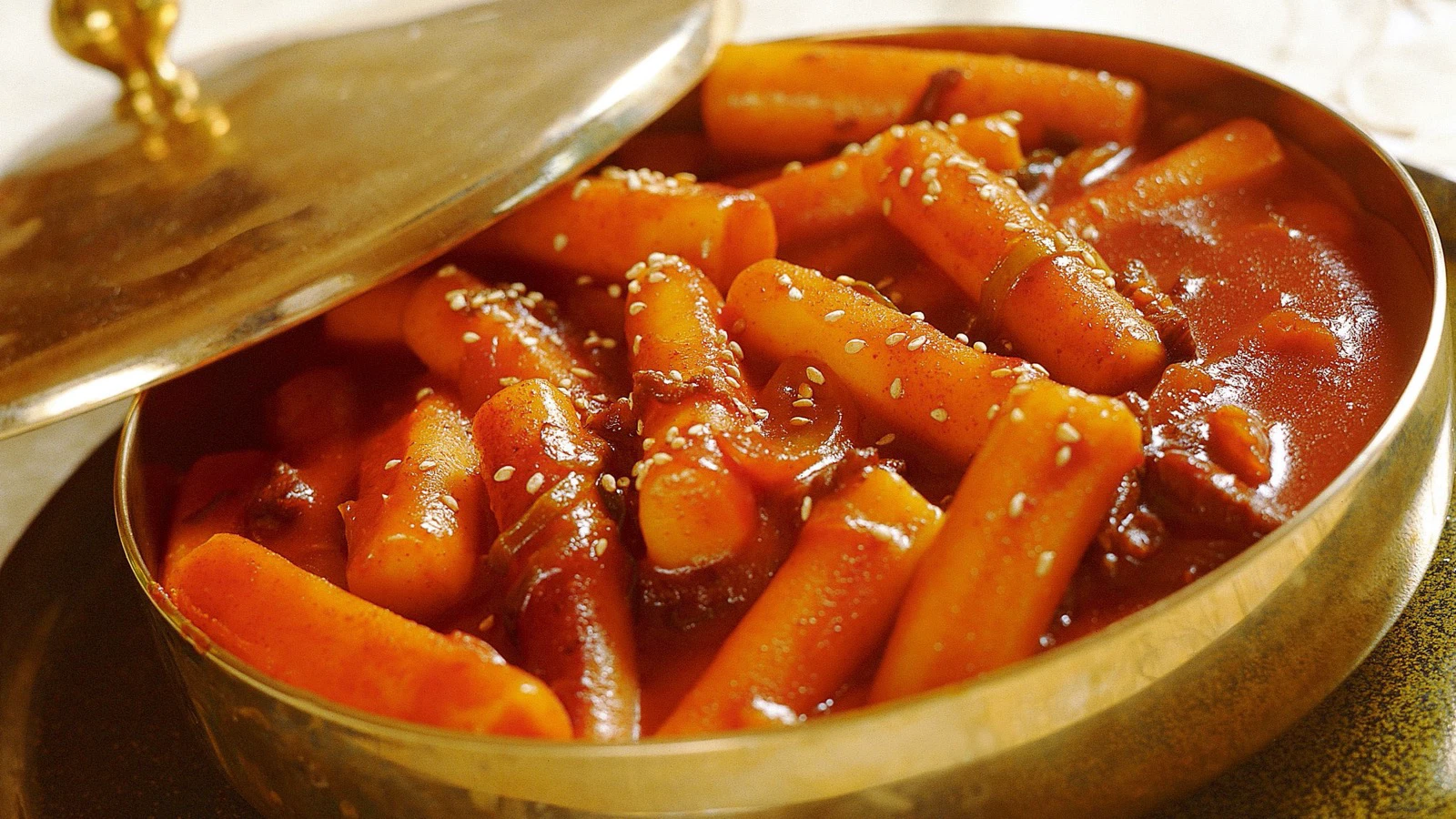 Red tteokbokki with cylindrical tteok in a shallow brass pan