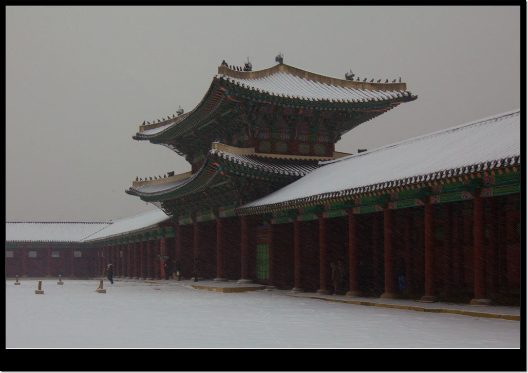Long tiled palace roofs and a quiet courtyard during snowfall at Gyeongbokgung Palace