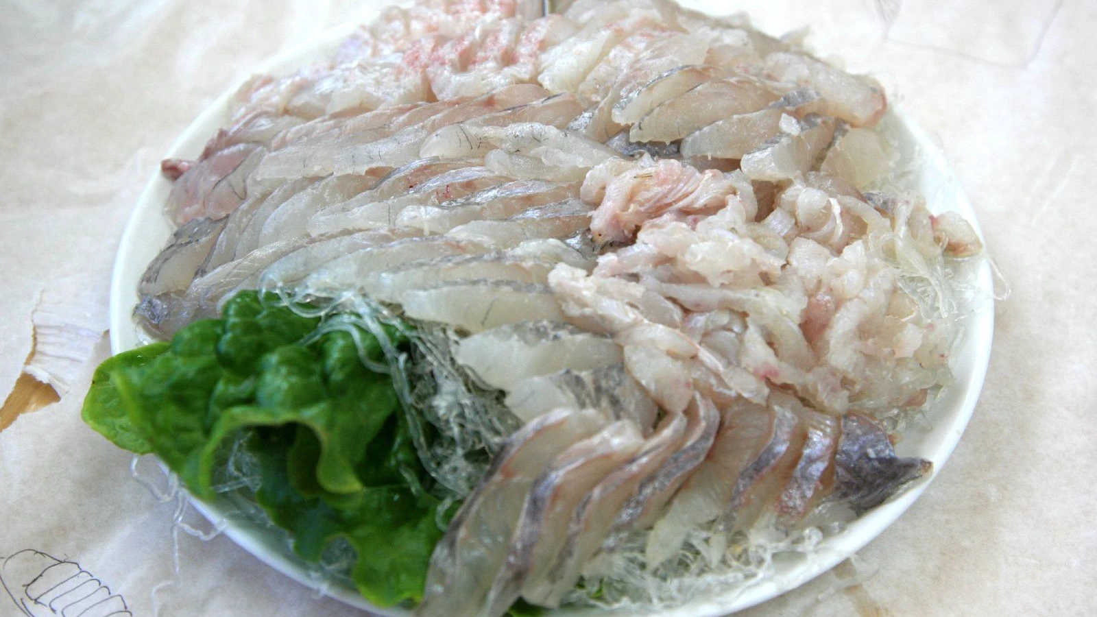 Thin translucent slices of Korean white-fish hwe arranged over shredded radish