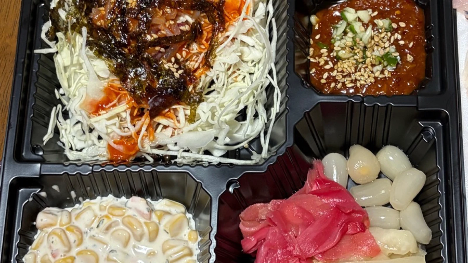 Takeout compartments with chojang, sliced garlic and side dishes served with Korean hwe