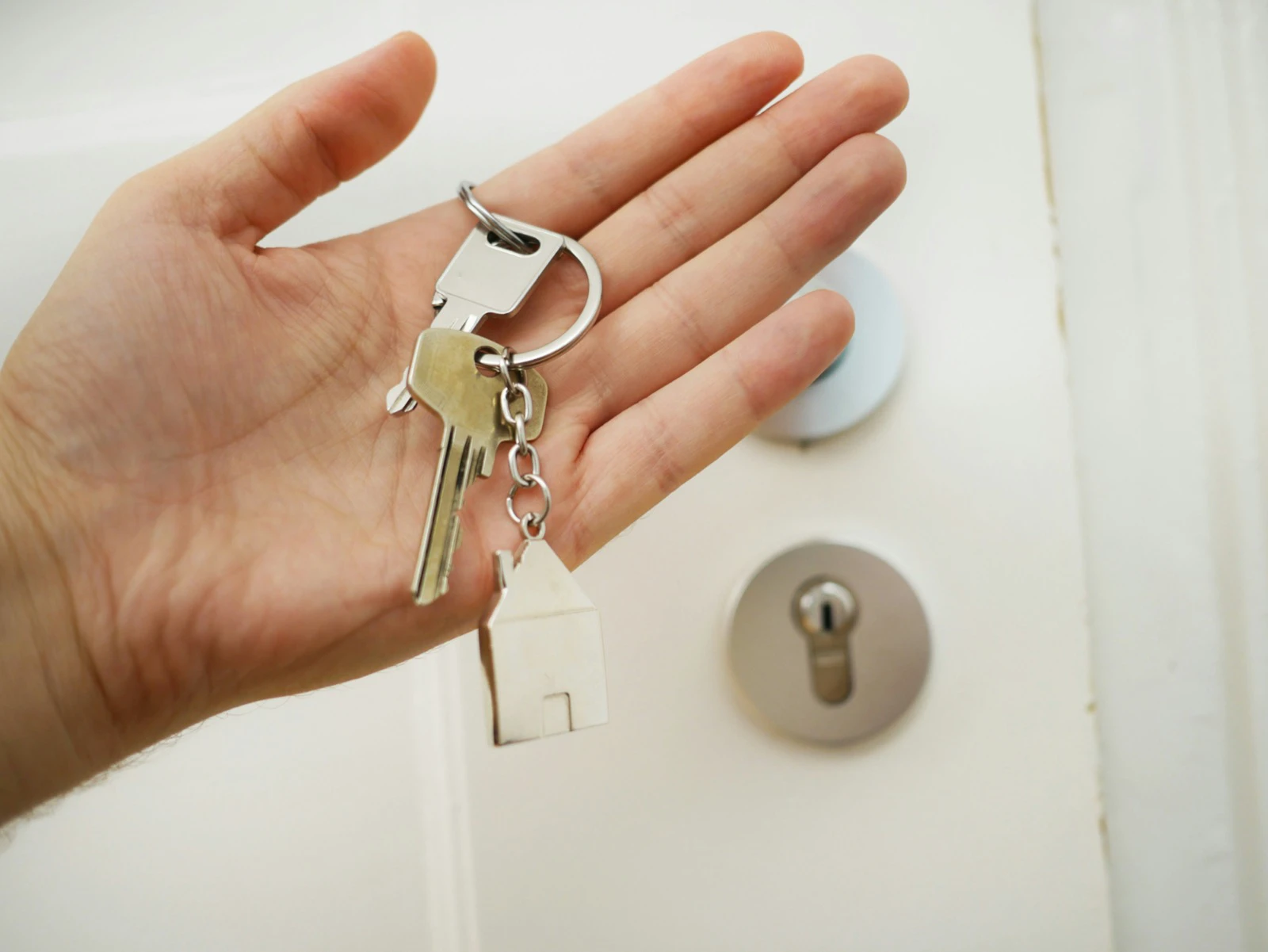 A hand holding several keys and a house-shaped keychain beside a door lock