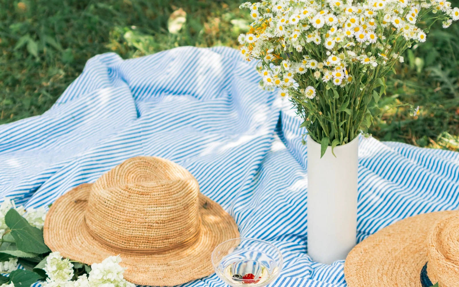 Striped picnic blanket with straw hats and flowers on grass