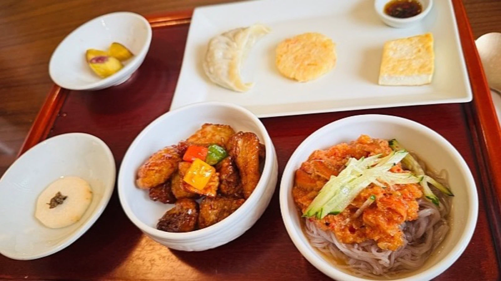Modern Korean temple-food course with noodles, glazed vegetables, tofu, dumpling, and small sides