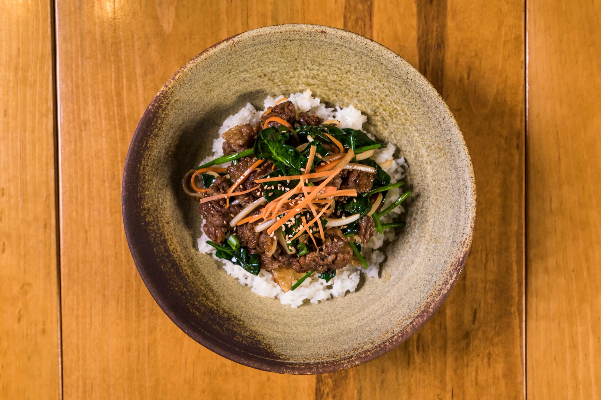 A single bulgogi rice bowl with vegetables on a wooden table