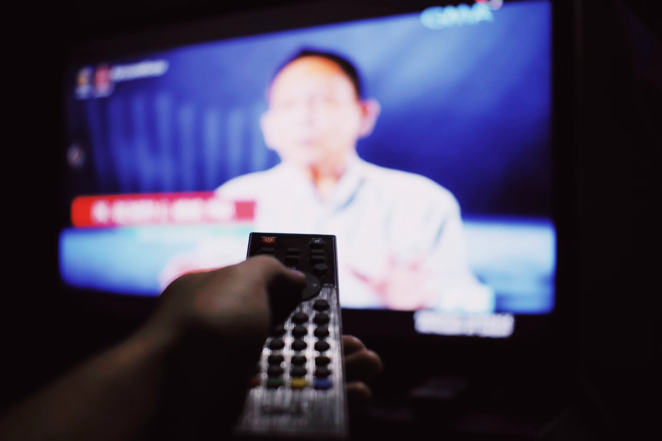 Tangan mengarahkan remote control ke layar televisi