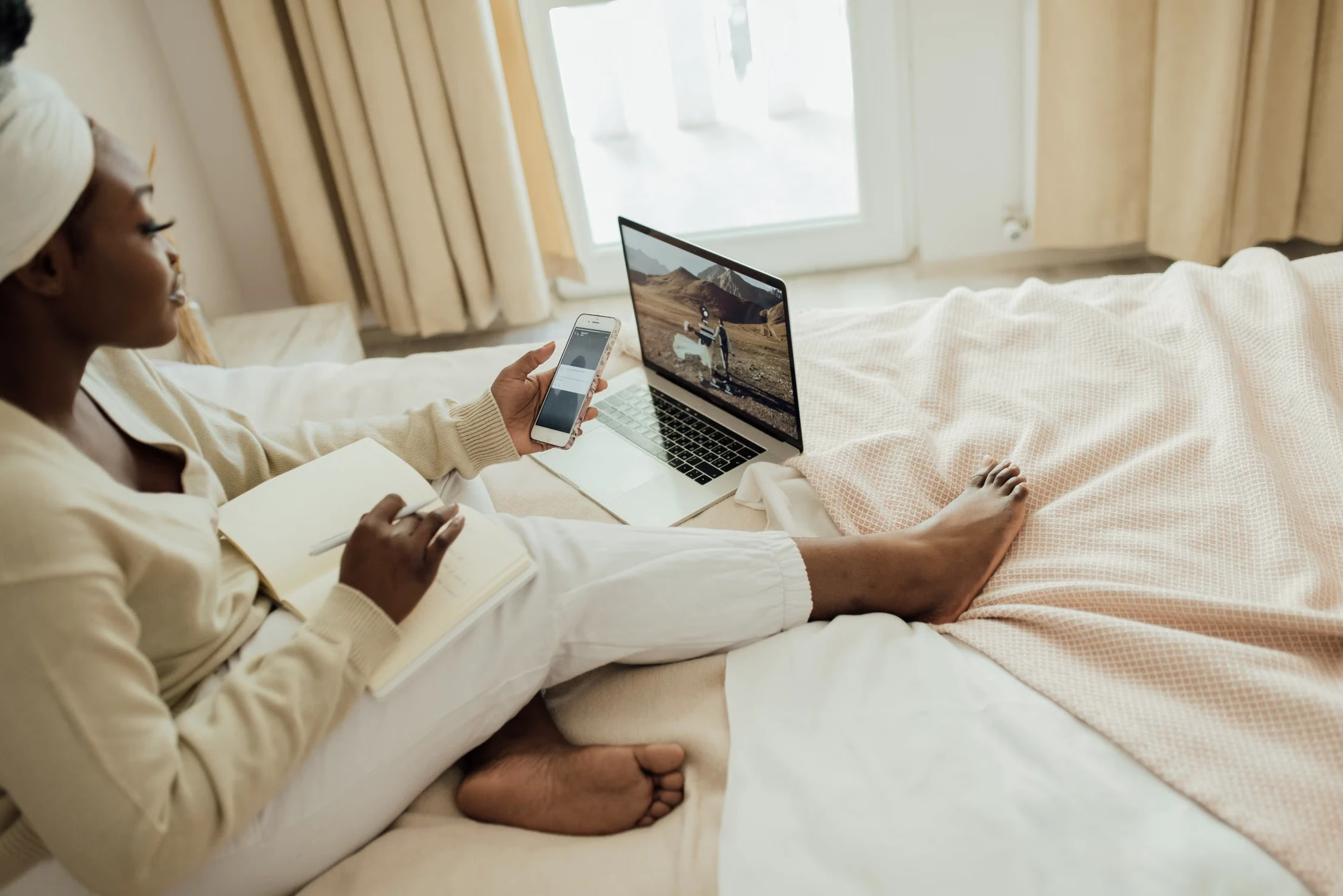 Seorang perempuan menonton video di laptop sambil menggunakan ponsel di rumah