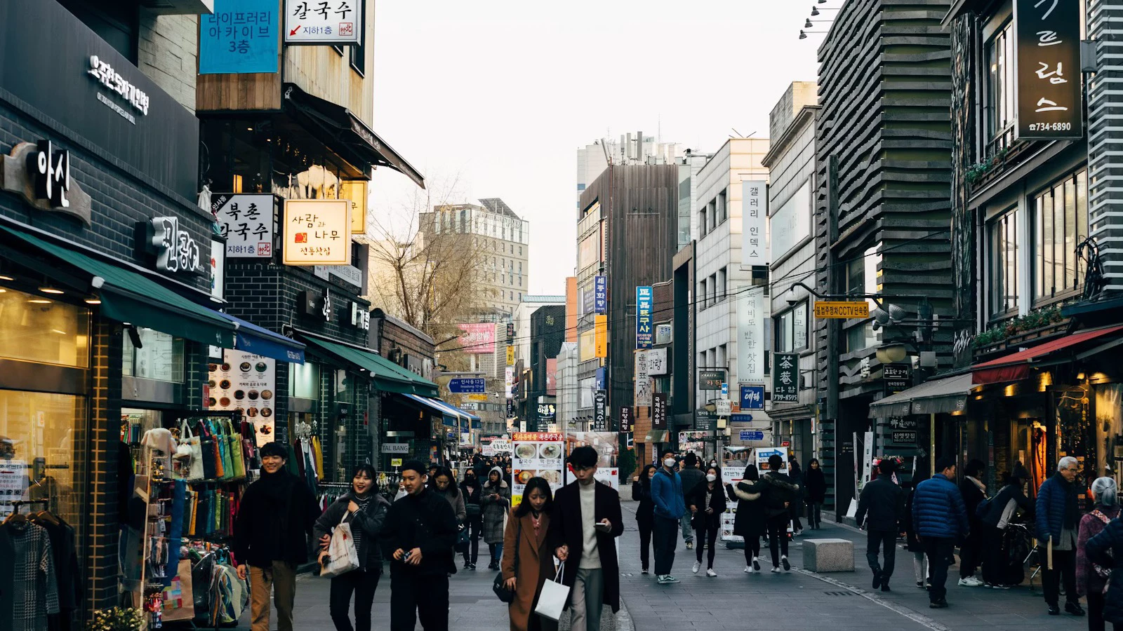 Pedestrians in coats and removable layers walking along a central Seoul street