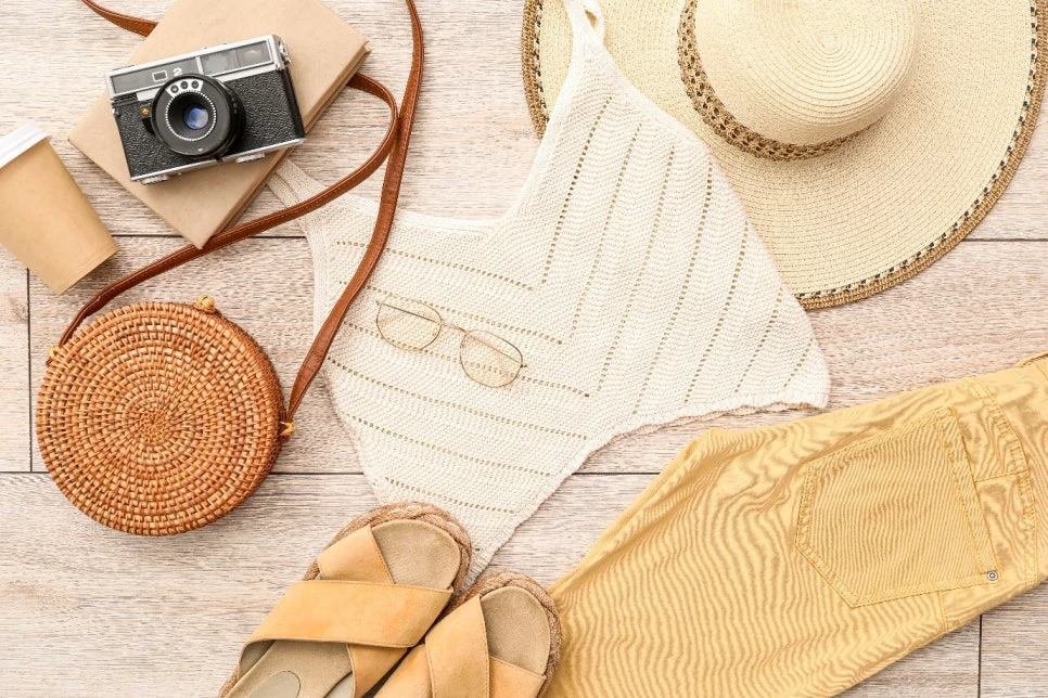Light summer clothing, sandals, and a sun hat arranged for warm-weather travel