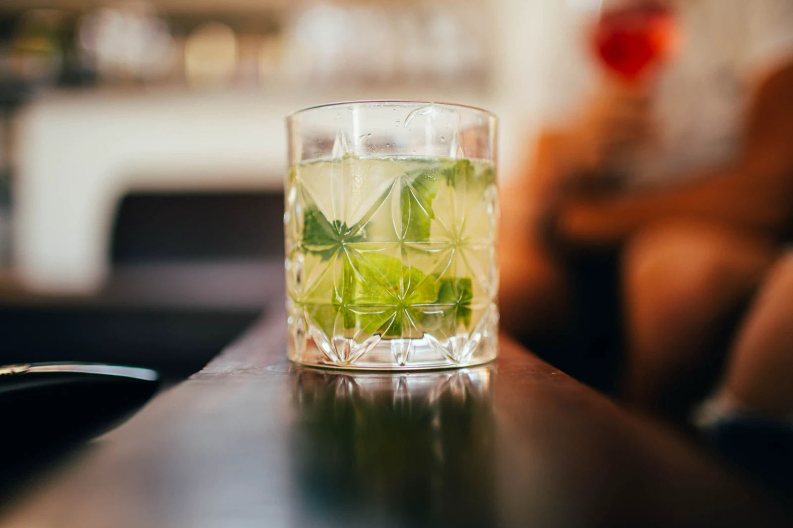 A single pale green cocktail rests on a polished bar counter