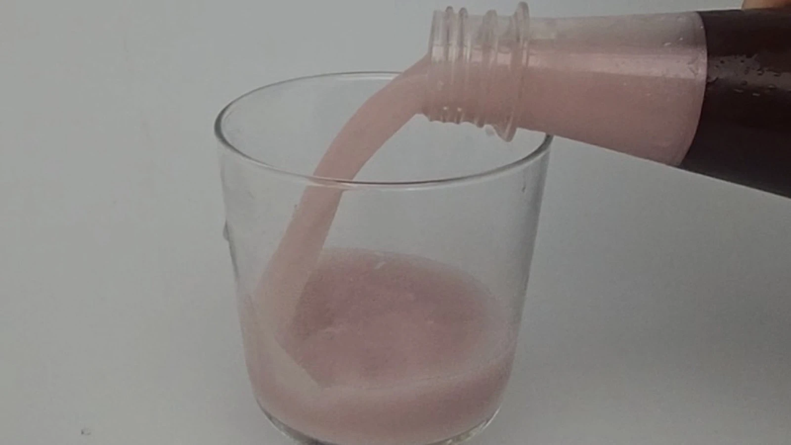 Pink live makgeolli being poured slowly from an open bottle into a clear glass