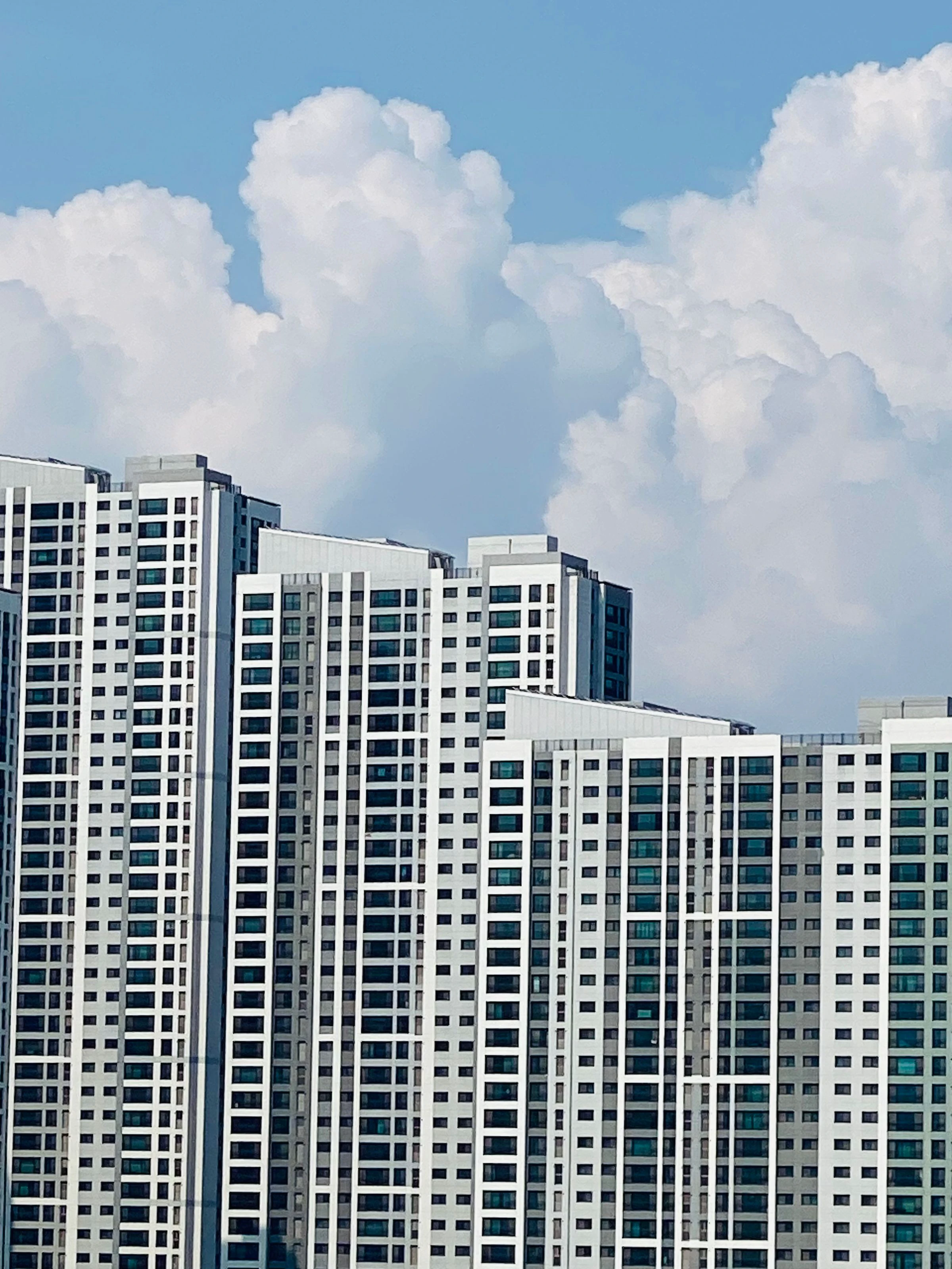Modern white high-rise apartment towers in Seoul beneath summer clouds