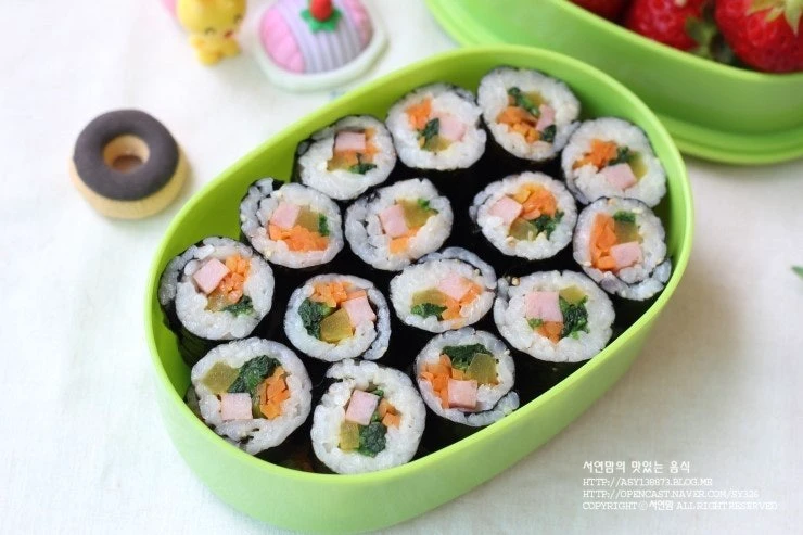 Gulungan gimbap kecil dalam kotak bekal hijau untuk piknik