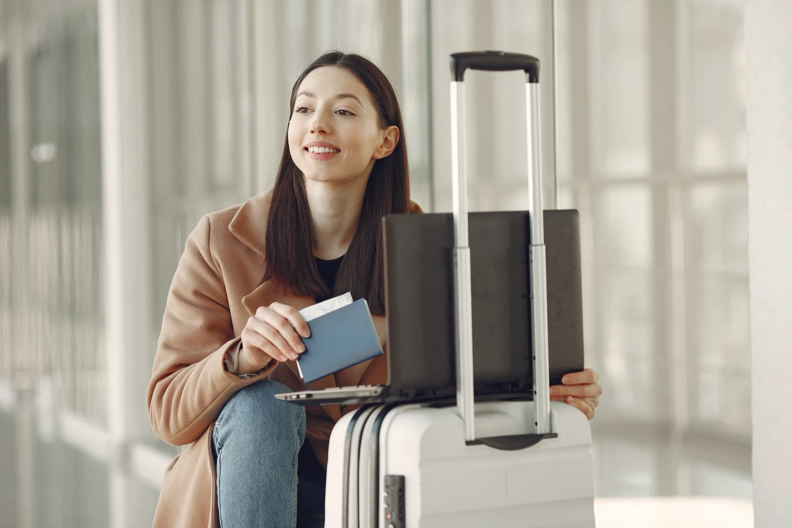 Solo young traveler holding a passport beside a suitcase in an airport