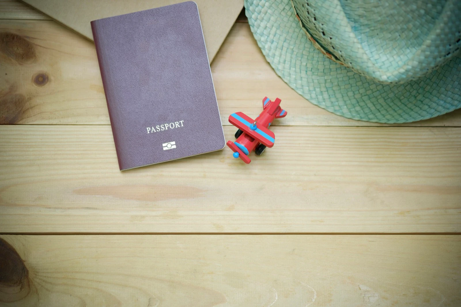 Closed passport beside a small airplane model and travel hat
