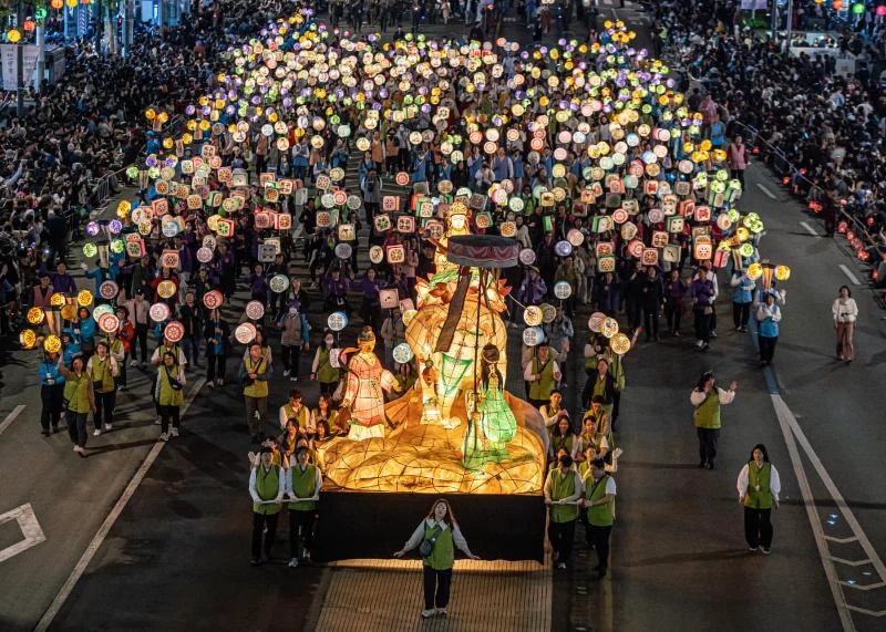 Registered participants carrying patterned handheld lanterns behind an illuminated float in Seoul’s Jongno parade