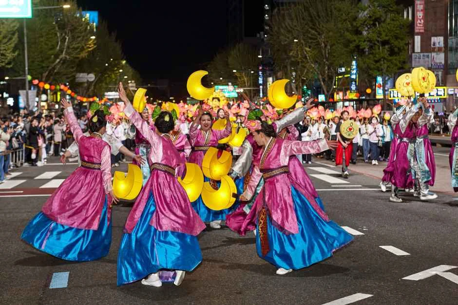 Performers in pink and blue traditional costumes dancing with glowing crescent lanterns during the Seoul parade