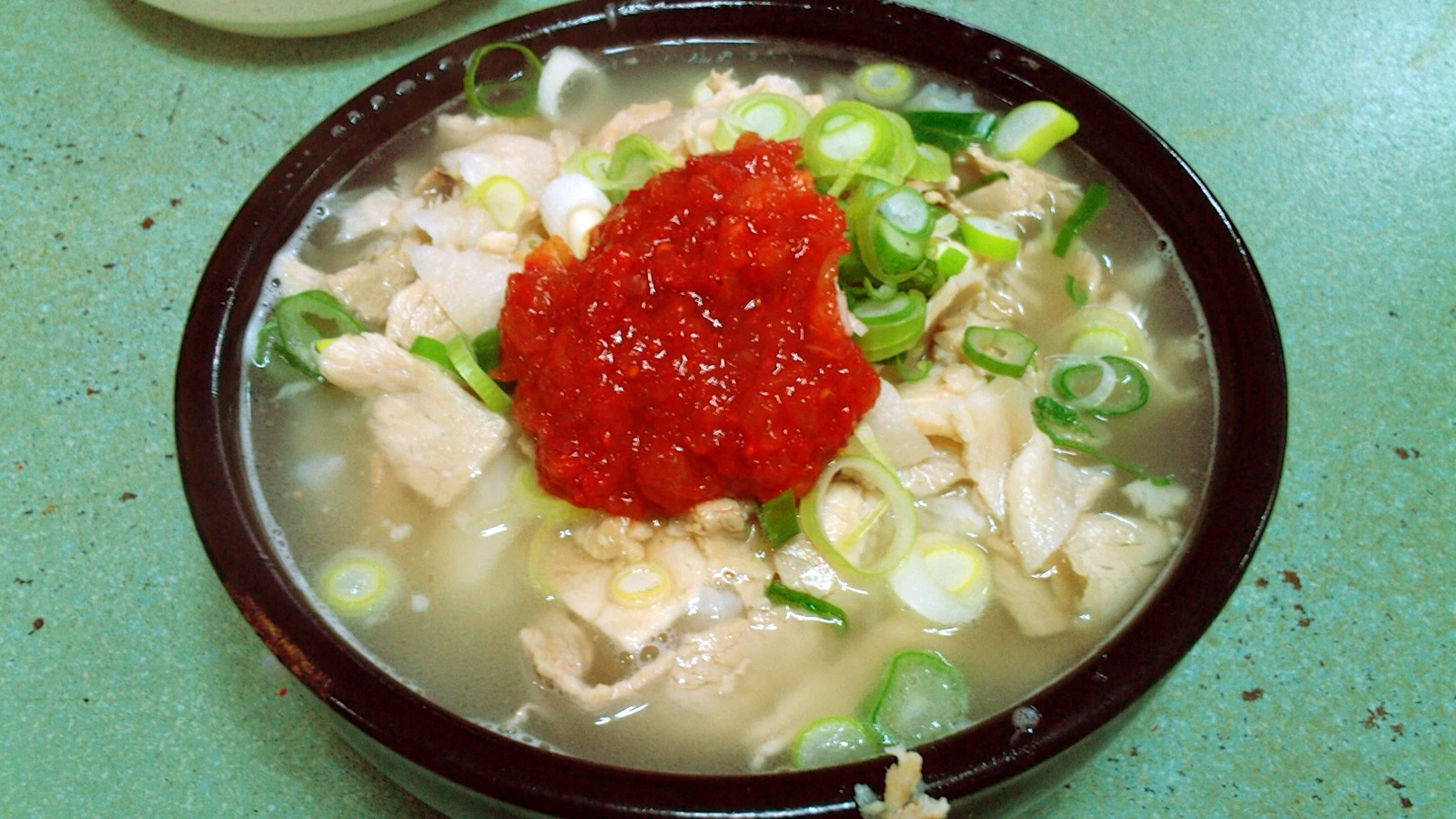Semangkuk sup nasi babi ala Busan mengepul dengan irisan daging dan daun bawang