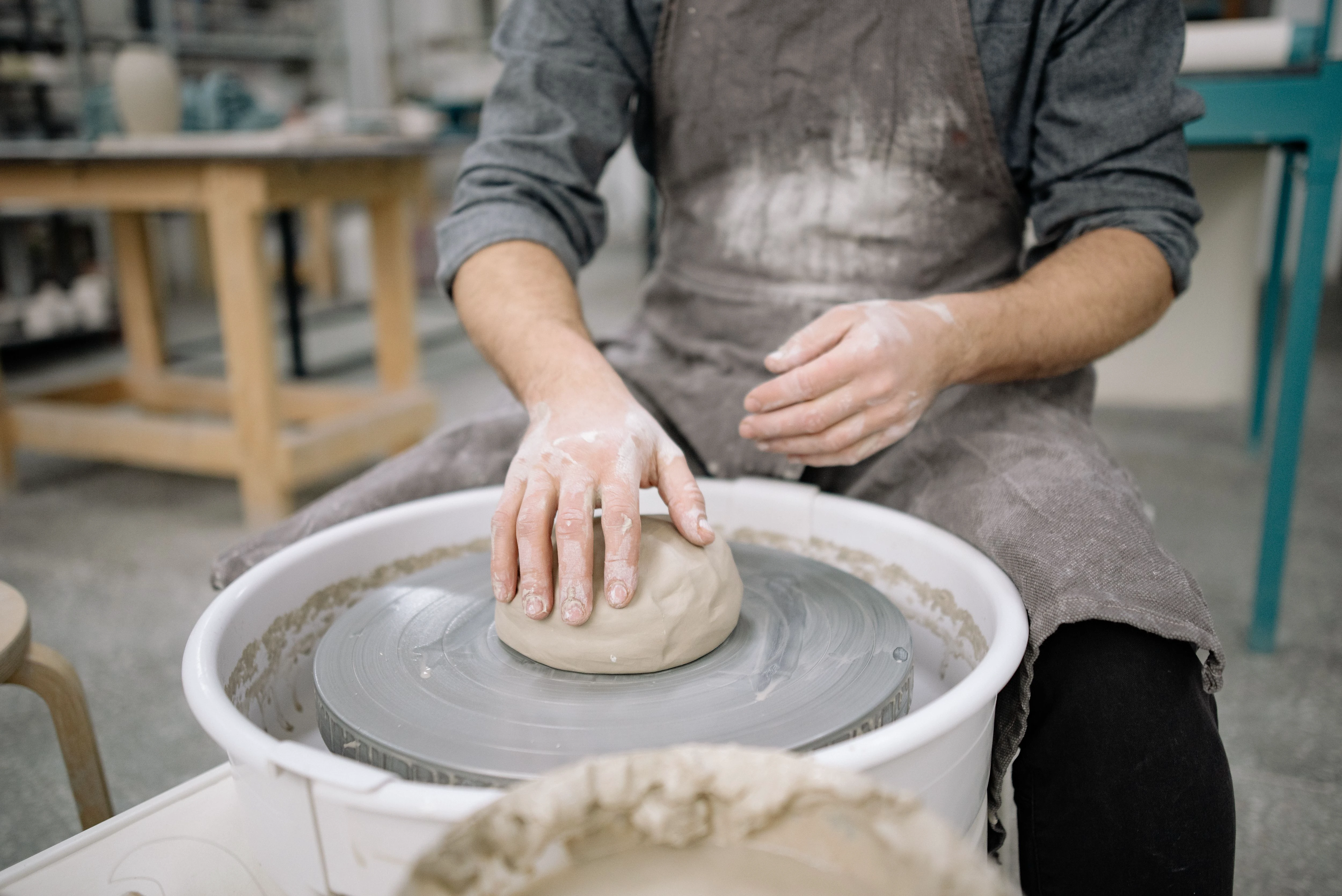 A potter centering a mound of clay on a spinning wheel in a workshop
