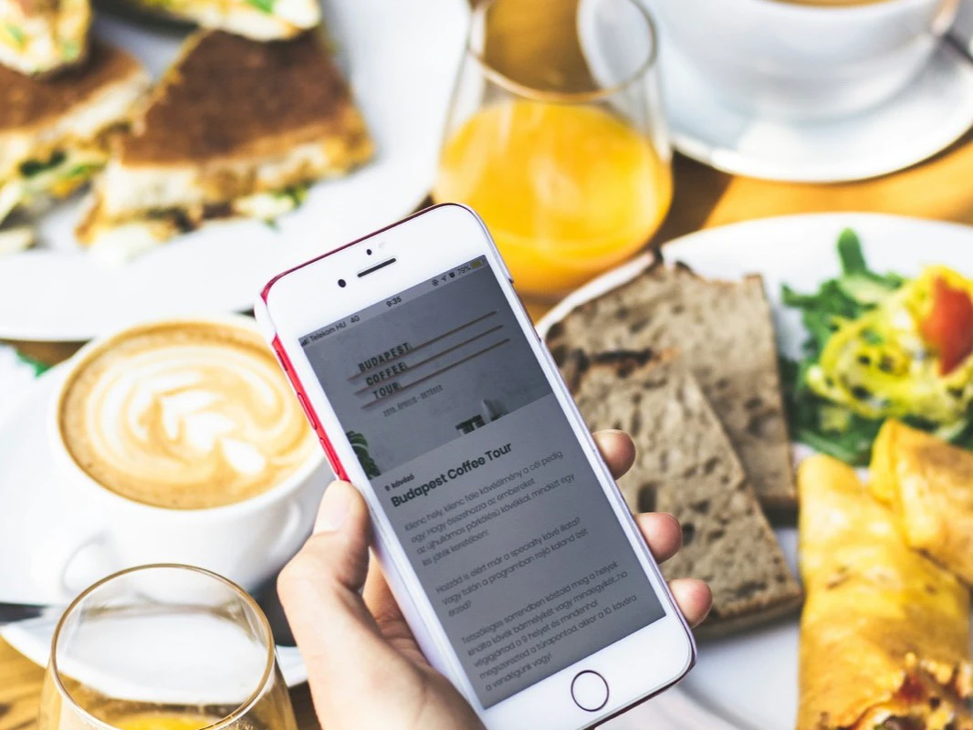 A person checking a phone over a carefully arranged cafe table with coffee and food