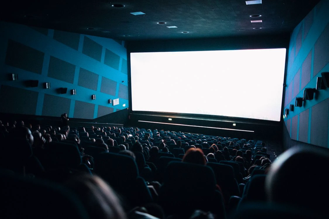 Penonton memenuhi bioskop menghadap layar besar yang menyala