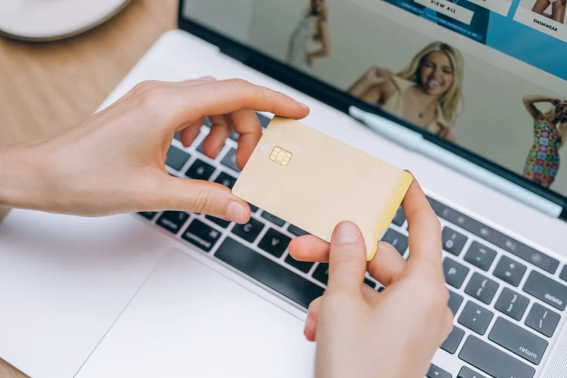 Hands holding a blank credit card above a laptop during online shopping
