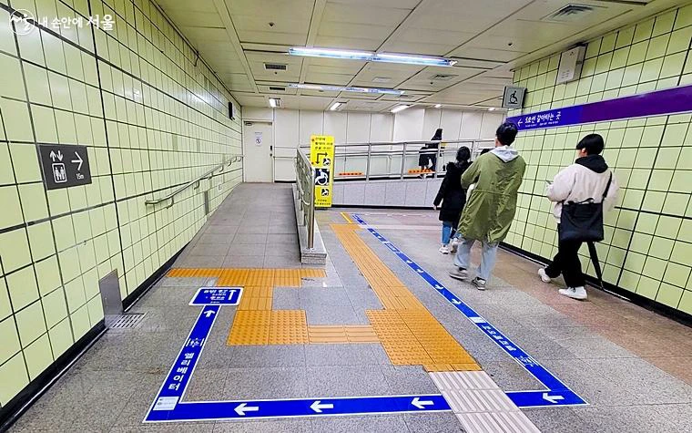 Blue elevator guidance line leading along a ramp inside a Seoul subway station