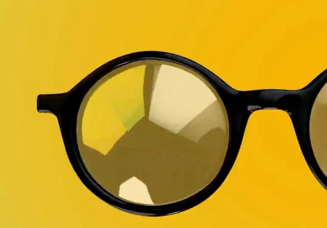 Close-up of a photochromic eyeglass lens changing tint on a yellow background