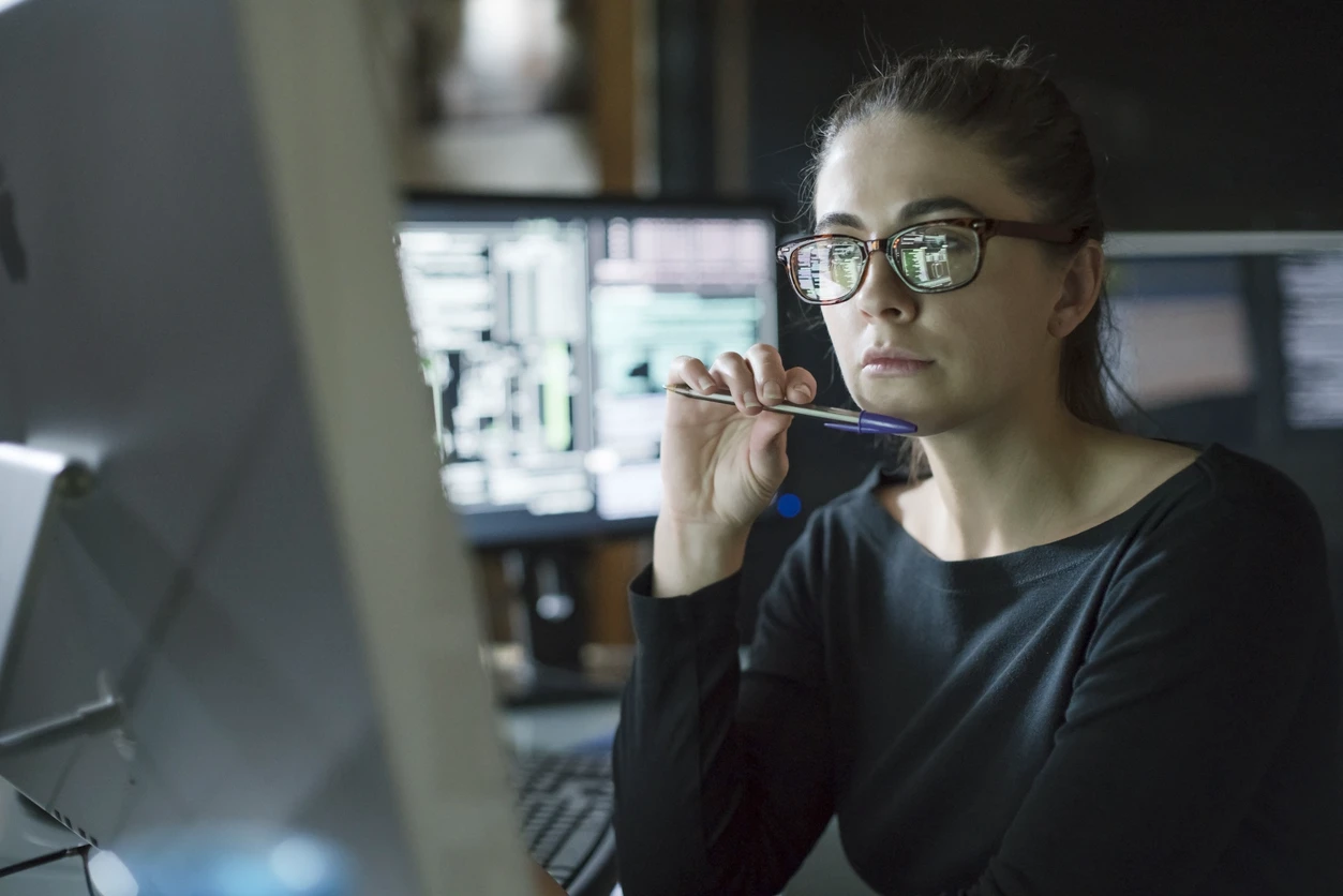 Person wearing glasses while working in front of several computer screens