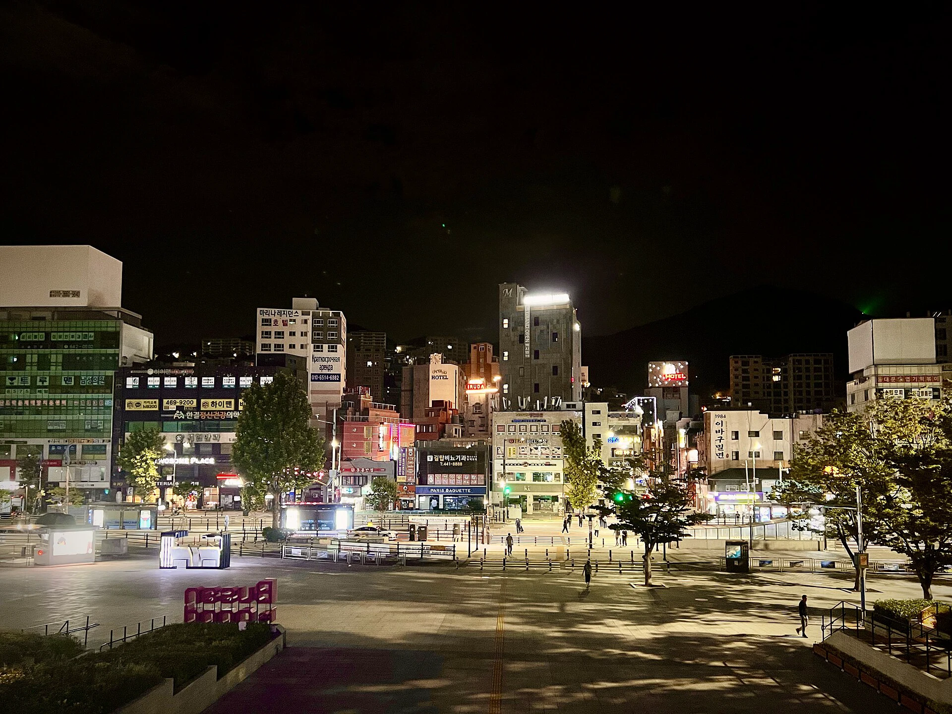 A brightly lit Busan street at night with illuminated signs and deep shadows