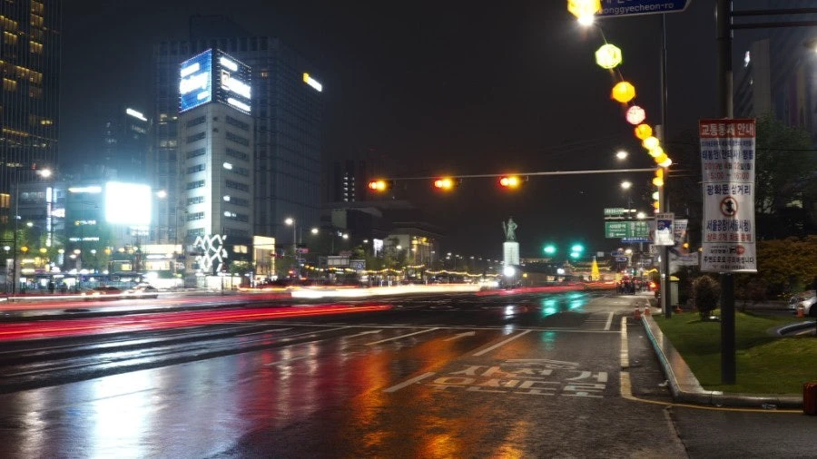 Red and green traffic lights reflected across a wet Seoul street at night