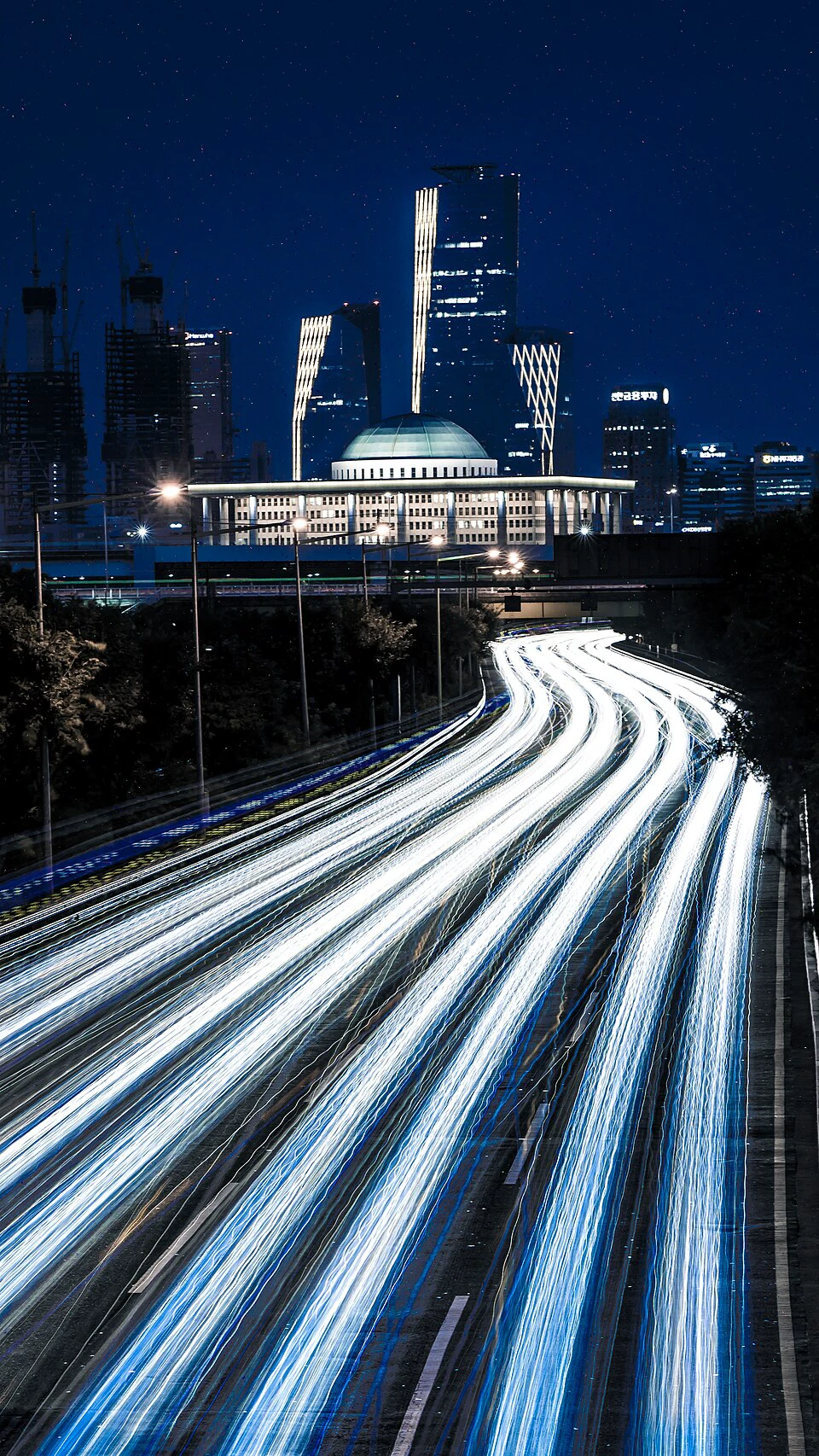 Long white and blue vehicle light trails curving past the National Assembly in Seoul