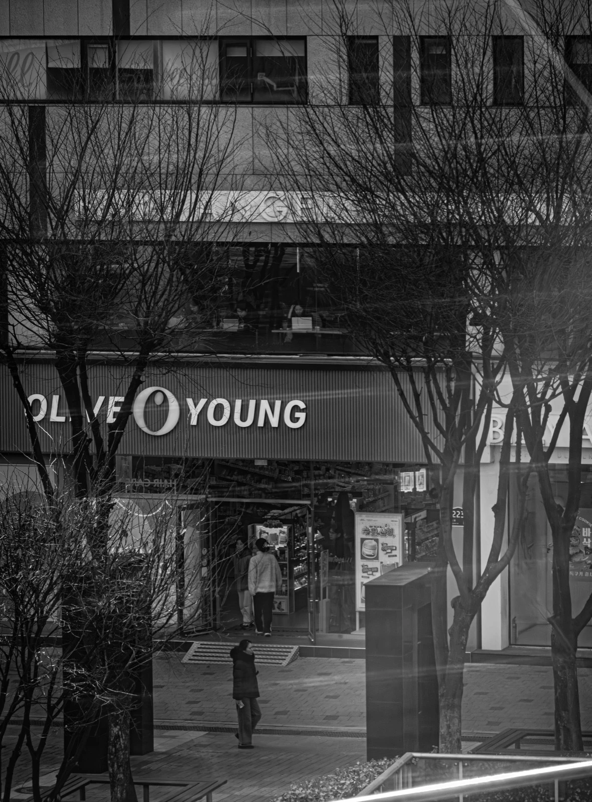 Black-and-white street view of a quieter Olive Young storefront in Seoul