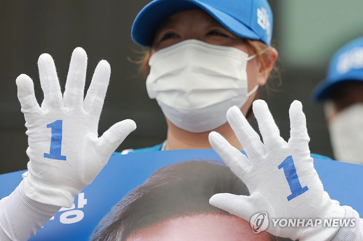A campaign worker holds up white gloves printed with ballot number one during the 2026 Korean local election