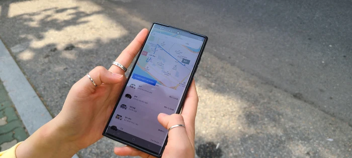 Person checking a taxi-hailing app on a phone beside a Seoul road